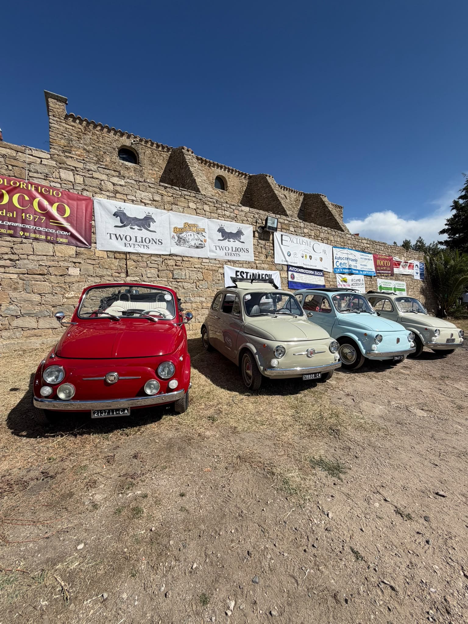 Row of classic Fiat 500s in front of the historic walls and Two Lions Events banners